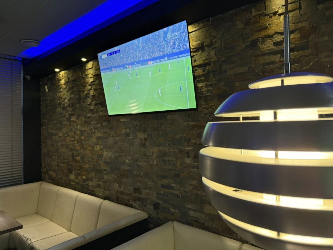Velkoplošná obrazovka s živým fotbalovým přenosem, kamenný obklad a modré LED osvětlení